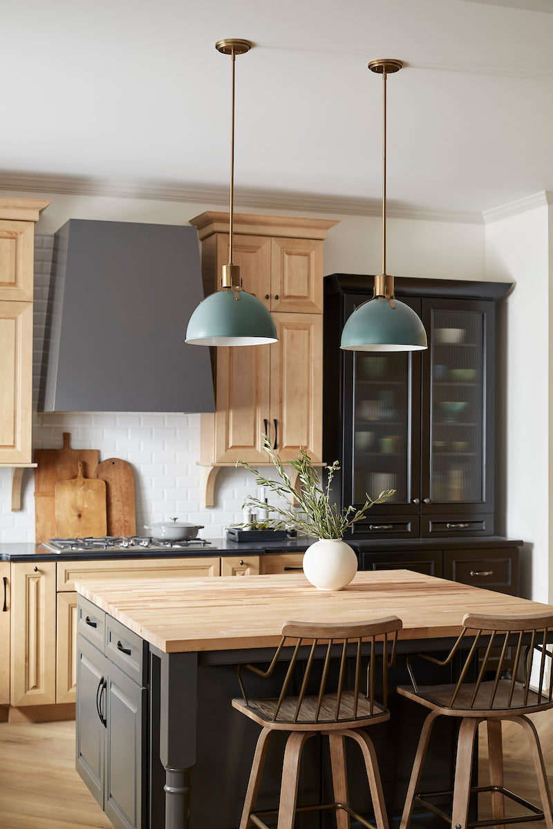 European farmhouse kitchen with mixed finish cabinets and butcher block counters. Green and gold metal pendants over island.